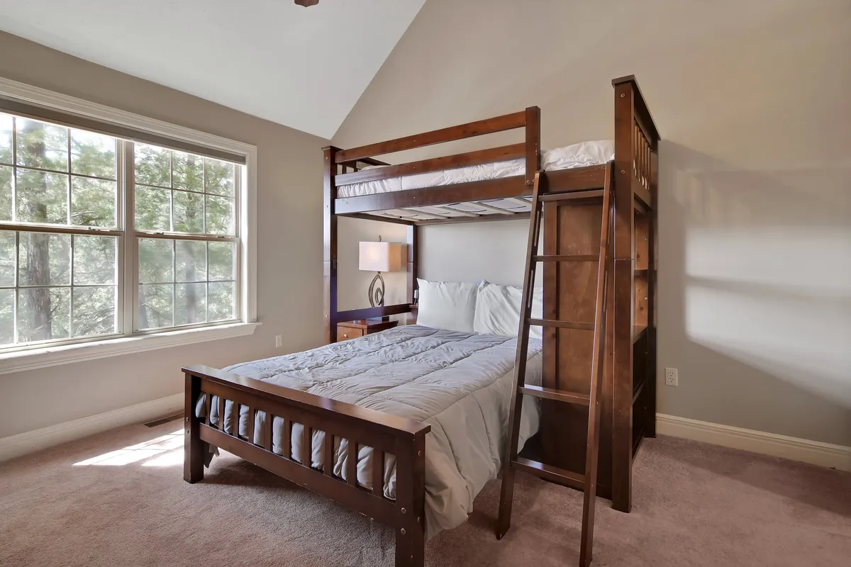 A welcoming family bedroom with a bunk bed, window, lamp, and bedside table. The space is bright and cozy, suitable for children or family groups, with thoughtful touches for comfort and relaxation.
