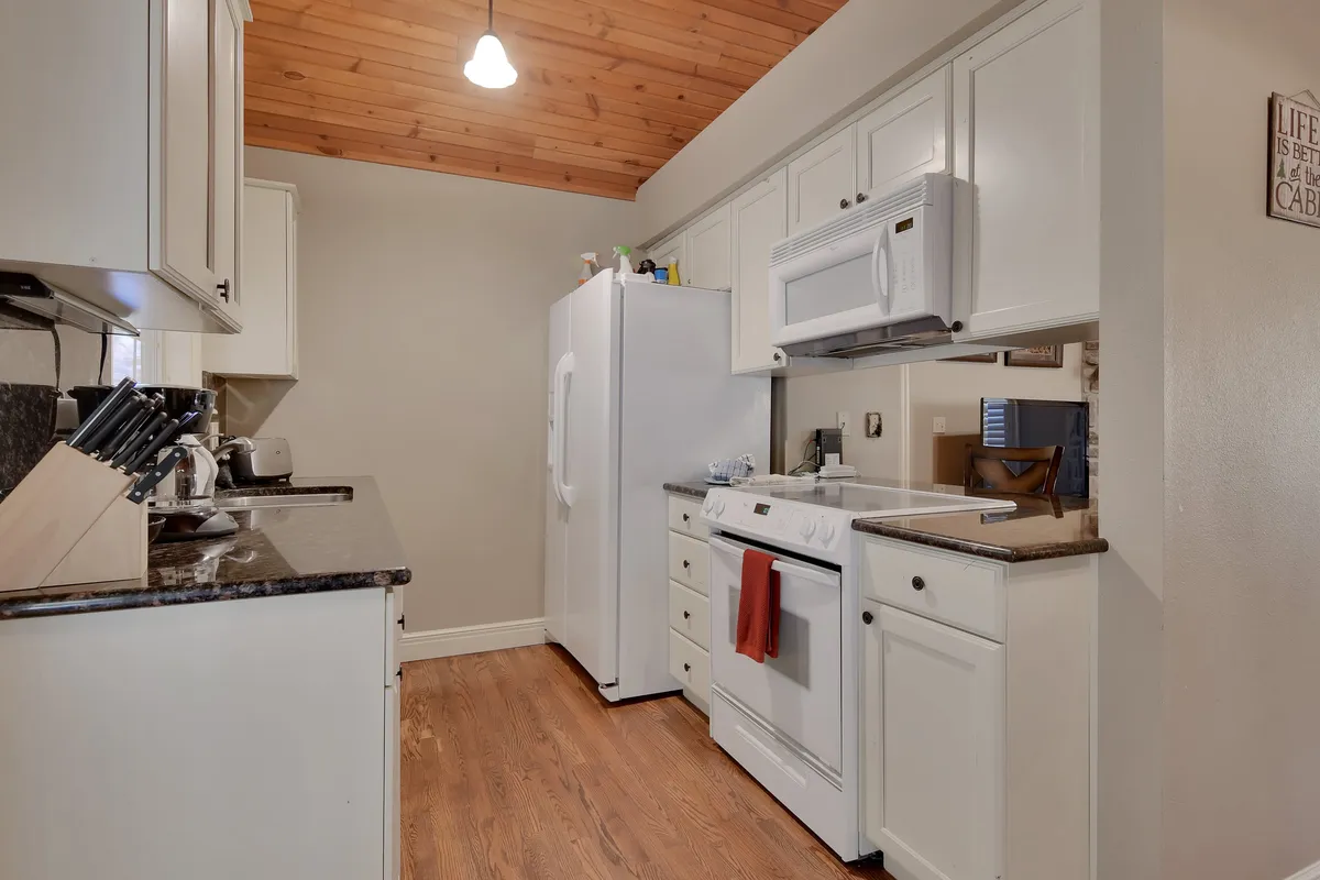 A view of a kitchen featuring granite countertops, white appliances, a wooden ceiling, and a selection of kitchen utensils. The space feels intimate and organized, ideal for preparing both everyday snacks and special meals.