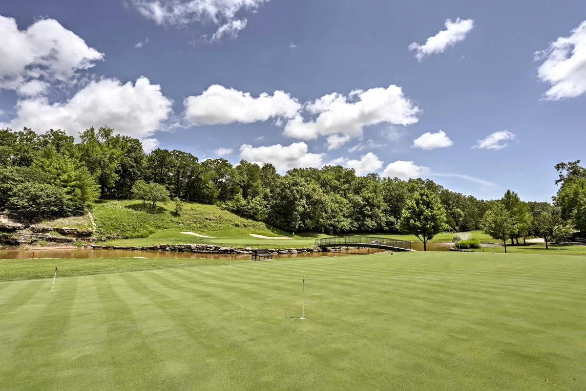 A peaceful golf green with a well-maintained bridge crossing over a water feature, surrounded by mature trees and lush landscaping. The scene is bathed in soft natural light, evoking the calm of an early morning or sunset round of golf.