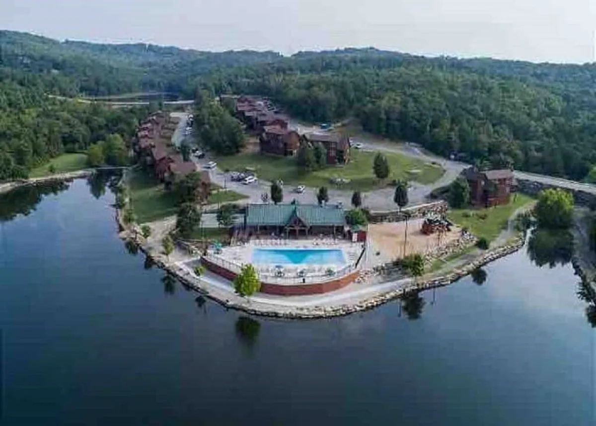 A sparkling outdoor swimming pool set against a rustic lodge backdrop, with views of a nearby lake and lush trees. Lounge chairs and picnic areas encourage relaxation and fun under the sun.