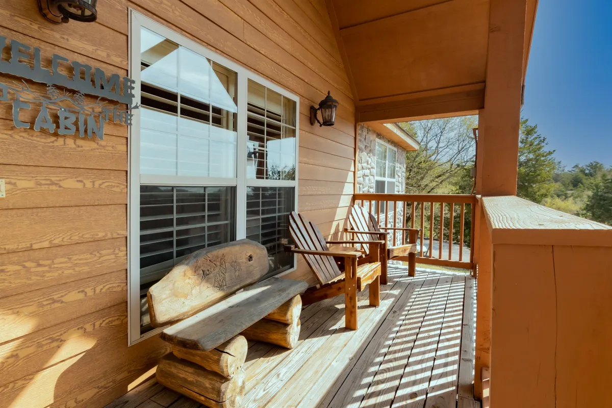 A cozy porch scene with a wooden bench, rocking chairs, and a welcoming cabin sign. The porch looks out onto nature and feels inviting for guests who want to relax outdoors with their pets after a day of exploration.