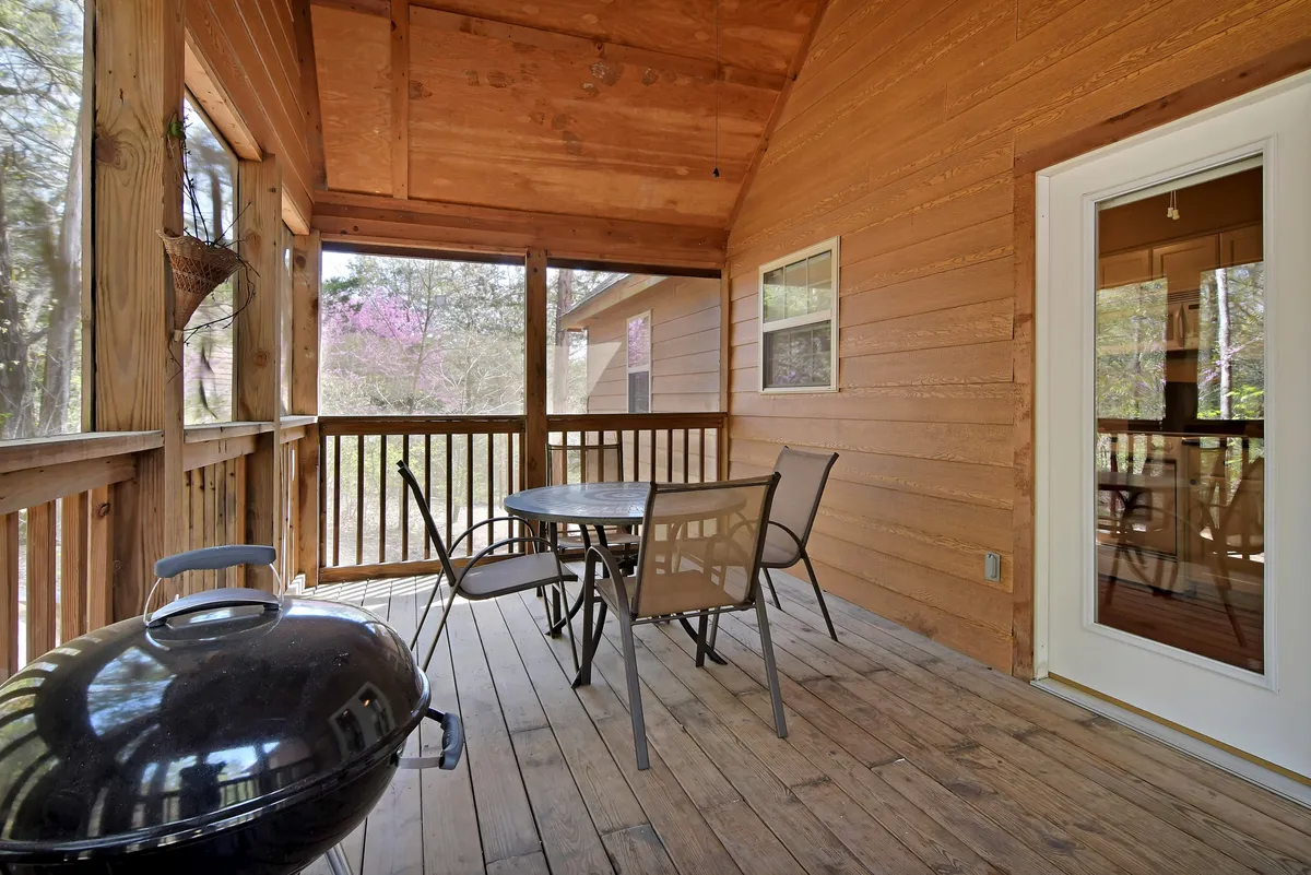 A spacious wooden deck set amidst lush greenery, featuring an outdoor dining table, a charcoal grill, and comfortable seating. The deck provides direct views of the surrounding natural landscape, inviting guests to gather for meals or relax in the fresh air. Subtle touches suggest the deck is perfect for morning coffee or evening stargazing.