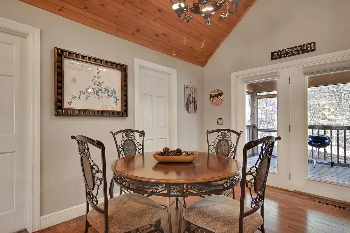 An inviting dining area with a round wooden table, ornate chairs, and a decorative chandelier overhead. Wall art adds character, while the arrangement suggests a space meant for shared meals, conversation, and connection.