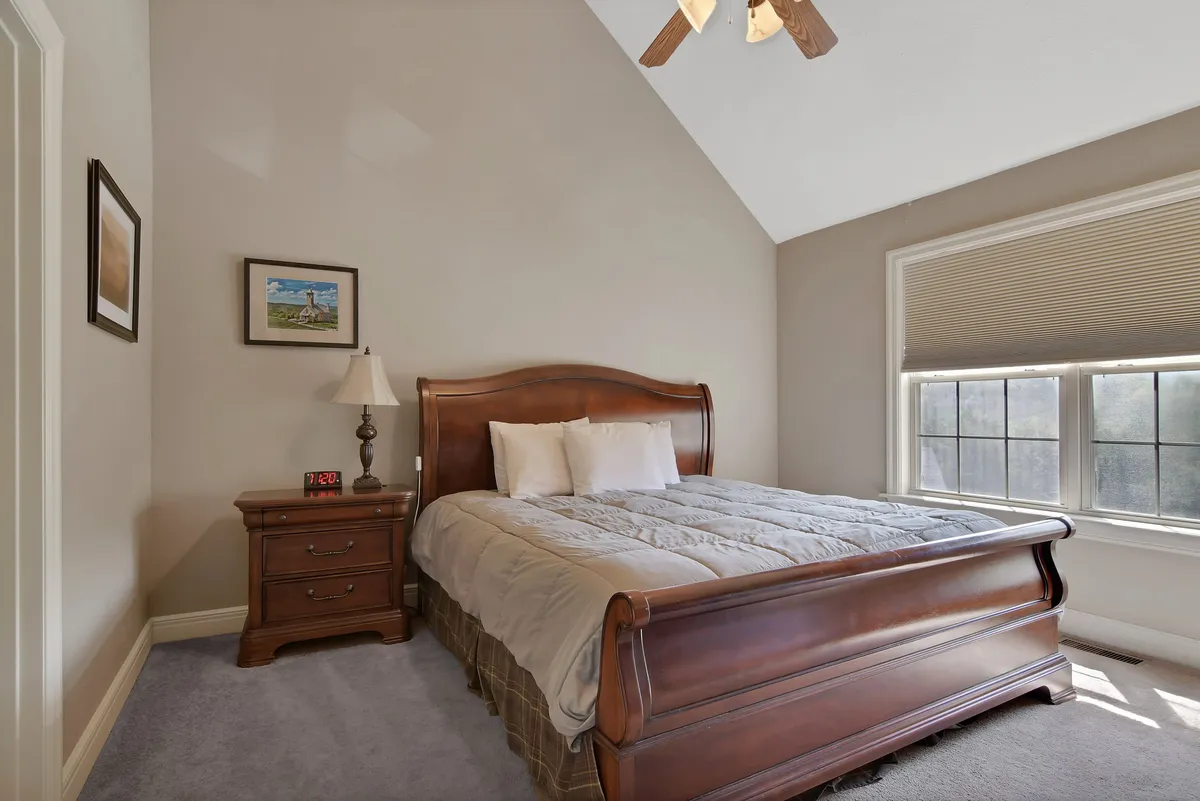 A serene bedroom centered around a sleigh bed, complemented by a nightstand and large window that lets in soft, natural light. Cozy blankets and subtle decor create an inviting sense of tranquility, ideal for restful sleep.